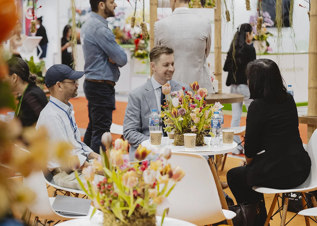 Delegates hold a business meeting surrounded by floral displays at HortEx, discussing trade opportunities.